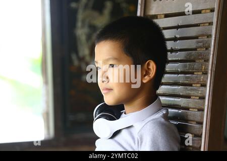 Un giovane ragazzo attento si siede in un ambiente interno accogliente, indossando le cuffie e godendosi un momento di relax e contemplazione. Ideale per temi di ch Foto Stock