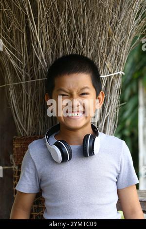 Un ragazzo allegro che indossa le cuffie sorride molto, irradiando gioia ed energia. Su uno sfondo naturale, questo ritratto cattura l'essenza del pla Foto Stock