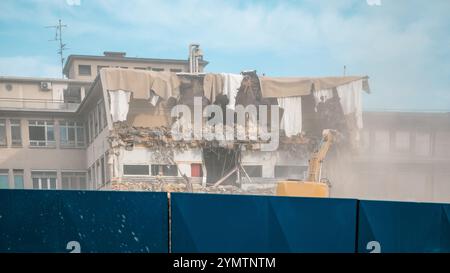 Demolizione di una casa industriale con demolitore e escavatore, lasciando spazio a nuovi edifici. Interno esposto della casa. Barriera in primo piano Foto Stock