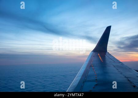 Vista serale dalla finestra dell'aereo. Il sole è tramontato dietro l'orizzonte. Le nuvole continue sono visibili sotto l'ala Foto Stock