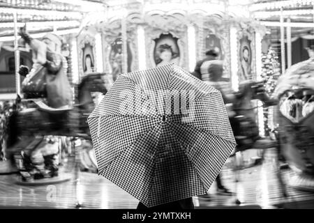 Foto in bianco e nero di una donna che tiene l'ombrello davanti ai cavalli rotanti della giostra. Giostra di notte in Piazza della Repubblica a Firenze Foto Stock