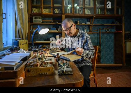 Radioamatore impegnato nella riparazione di un ricevitore radio. Sulla tabella sono riportati gli attrezzi per la riparazione Foto Stock