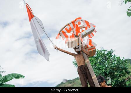 Il ragazzo sale e alza la bandiera indonesiana vincendo la gara di arrampicata con le areca Foto Stock