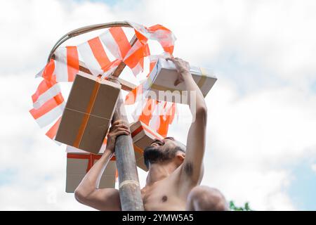 l'uomo afferra un premio in scatola di cartone durante una gara di arrampicata su betel nut Foto Stock