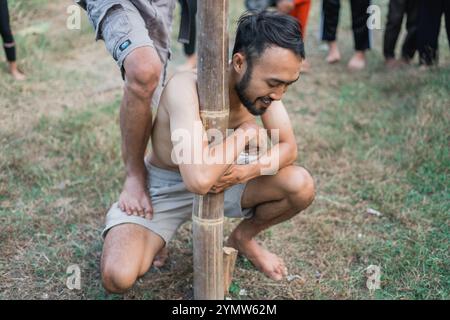 L'uomo barbuto abbraccia un palo mentre partecipa alla celebrazione dell'indipendenza indonesiana dell'arrampicata areca Foto Stock