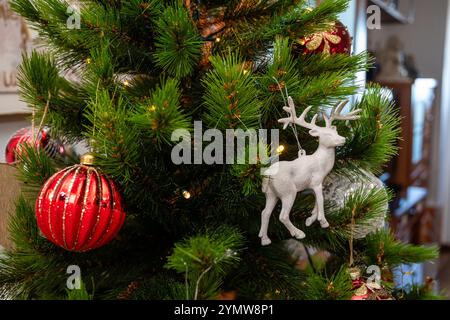 Un albero di Natale con un ornamento di cervi bianco appeso ad esso. L'albero è decorato con molti ornamenti, tra cui una palla rossa e un ornamento rosso e bianco Foto Stock