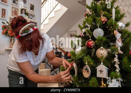 Una donna sta decorando un albero di Natale con ornamenti. Indossa una camicia bianca e un cerchietto rosso Foto Stock