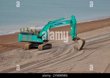 Paesaggio di veicoli per impianti pesanti Seaford Shingle Beach escavatore terna turchese cingolato cingolo lungo braccio idraulico e benna Foto Stock