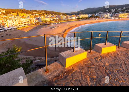 Vista mattutina della baia, spiaggia sabbiosa circondata da colline boscose a Tossa de Mar all'alba, in Spagna Foto Stock