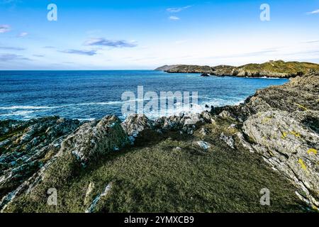 Il sole tramonta all'orizzonte, illuminando le aspre scogliere accanto al mare tranquillo. Le onde si infrangono dolcemente contro le rocce, creando una costa tranquilla Foto Stock