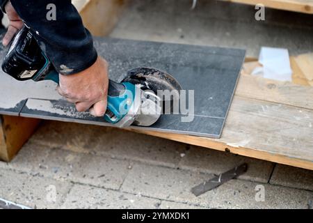 Uomo che utilizza una smerigliatrice angolare a batteria per tagliare piastrelle in ceramica Foto Stock