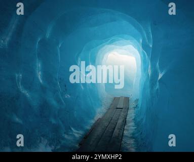 All'interno del ghiacciaio Rhône. Luce alla fine della grotta di ghiaccio blu. Passerella in legno nel tunnel all'interno di un ghiacciaio. Foto Stock