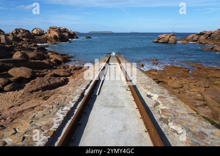 Un sentiero in pietra conduce attraverso un paesaggio costiero roccioso al mare blu sotto un cielo limpido, Cale de Porz-Kamor, scalo Porz-Kamor per scialuppe di salvataggio, Ploumana Foto Stock