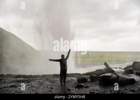 Dietro la maestosa cascata islandese: I turisti che catturano la bellezza di Seljalandsfoss si stagliano contro la nebbia e lo spruzzo in un iconico Natur islandese Foto Stock