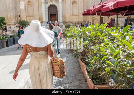 La Valletta Malta, St John's Square, Misrah San Gwann, donne donne femminili, camminate pedonali, indossando un cappello da sole floppy a tegole larghe, tessuto di paglia, St. John's Co Foto Stock