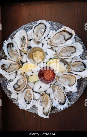 Ostriche fresche su ghiaccio con spicchi di limone e salse, servite elegantemente per un'esperienza culinaria a base di pesce Foto Stock