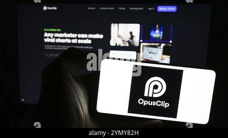 Stoccarda, Germania, 03-13-2024: Persona che detiene un telefono cellulare con il logo della società di video editing di intelligenza artificiale Opus Clip davanti alla pagina web. Foto Stock