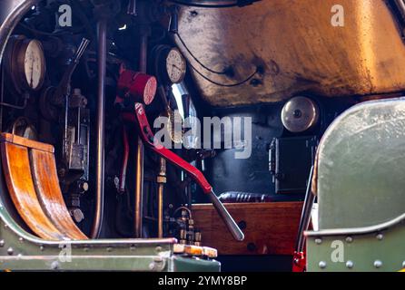 Primo piano del pannello di controllo in una locomotiva a vapore d'epoca con leve, indicatori e maniglia verniciata di rosso in un ambiente industriale Foto Stock