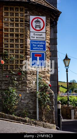 Cartello segnaletico in un pittoresco villaggio che mostra restrizioni stradali e una vista panoramica con lampione e fiori in fiore lungo un muro di pietra Kingswear Dartmouth Foto Stock