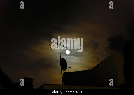 Luna piena in un cielo nuvoloso rosso che illumina un'antenna televisiva sul tetto Foto Stock