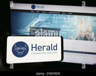 Stoccarda, Germania, 03-19-2024: Persona che detiene uno smartphone con logo della società britannica Herald Investment Trust plc davanti al sito web. Concentrati sul telefono Foto Stock