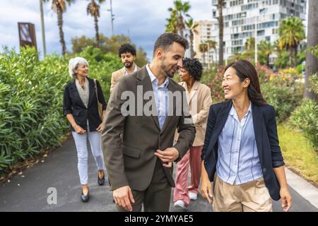Uomini d'affari rilassati e multirazziali che camminano lungo i giardini di un quartiere finanziario in una città tropicale Foto Stock
