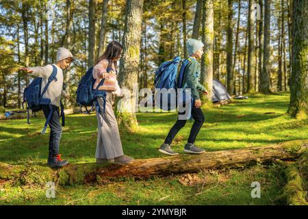 Foto a figura intera di due fratelli caucasici e una sorella che camminano su un tronco di albero morto mentre camminano nella foresta alpina Foto Stock