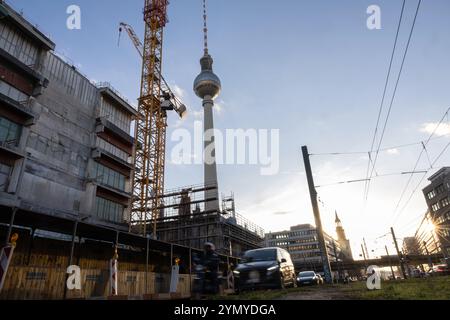 Berlino, Germania. 23 novembre 2024. Gli utenti della strada guidano di fronte a un cantiere in Alexanderplatz. La torre della televisione di Berlino e le gru da costruzione sono visibili sullo sfondo. Crediti: Hannes P. Albert/dpa/Alamy Live News Foto Stock