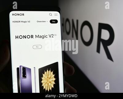 Stoccarda, Germania, 03-15-2024: Persona che detiene un telefono cellulare con pagina Web della società cinese di smartphone Honor Device Co. Ltd. Davanti al logo. Concentrati Foto Stock