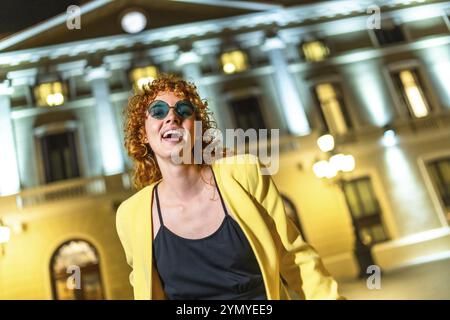 Bella donna sorridente alla macchina fotografica mentre balla per le strade della città di notte Foto Stock