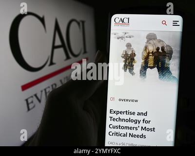 Stoccarda, Germania, 04-28-2024: Persona che detiene il cellulare con pagina web della società americana di tecnologie dell'informazione CACI International Inc. Con logo. Concentrati su Foto Stock