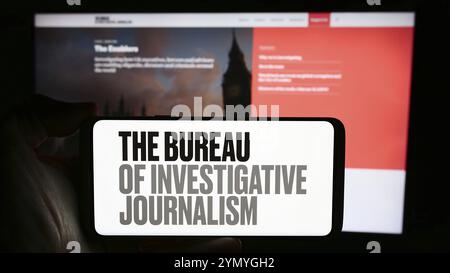 Stoccarda, Germania, 04-13-2024: Persona che detiene il cellulare con il logo dell'organizzazione il Bureau of Investigative Journalism (TBIJ) di fronte alla pagina web. Foto Stock