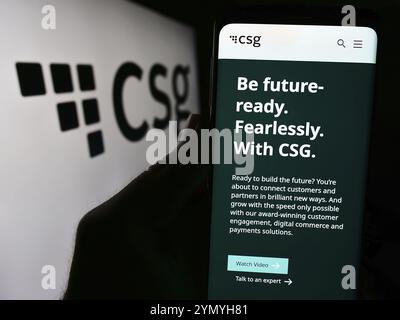 Stoccarda, Germania, 04-18-2024: Persona che possiede uno smartphone con pagina web della società di software BSS statunitense CSG Systems Inc. Davanti al logo aziendale. Concentrati su Foto Stock