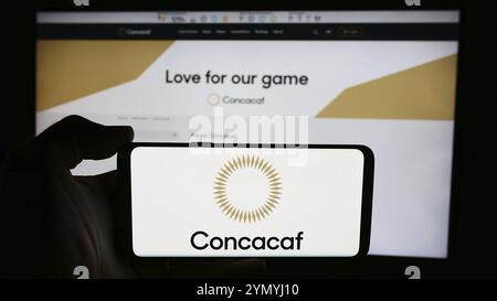 Stoccarda, Germania, 06-25-2024: Persona che tiene il cellulare con il logo dell'associazione calcistica CONCACAF davanti alla pagina web. Focus sul display del telefono, Europ Foto Stock