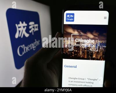 Stoccarda, Germania, 06-26-2024: Persona che detiene un telefono cellulare con il sito web della società di investimento Chenghe Group Ltd. Di fronte al logo aziendale. Concentrati su Foto Stock