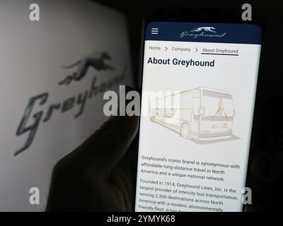 Stoccarda, Germania, 03-05-2024: Persona che possiede uno smartphone con pagina web della compagnia di autobus a lunga percorrenza Greyhound Lines Inc. Davanti al logo. Concentrati su Foto Stock