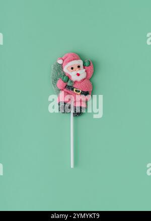 Composizione natalizia realizzata con lecca lecca di Babbo Natale su sfondo verde pastello. Concetto minimalista di caramelle dolci di Natale e Capodanno. C Foto Stock