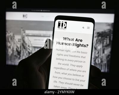 Stoccarda, Germania, 04-13-2024: Persona che detiene un cellulare con pagina web e logo della ONG di difesa legale detenuti internazionali davanti al monitor. Concentrati Foto Stock