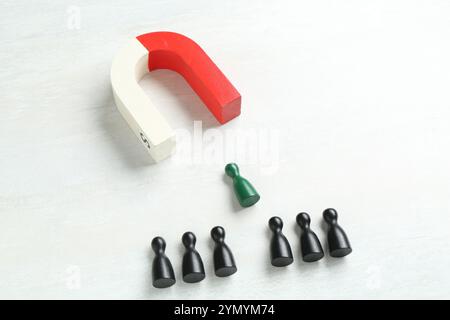 Magnete che attrae un pezzo verde tra quelli neri sul tavolo bianco Foto Stock