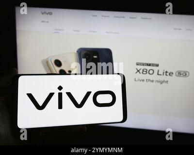 Stoccarda, Germania, 03-17-2024: Persona che detiene uno smartphone con il logo della società cinese vivo Communication Technology Co. Ltd. Davanti al sito web. FOC Foto Stock