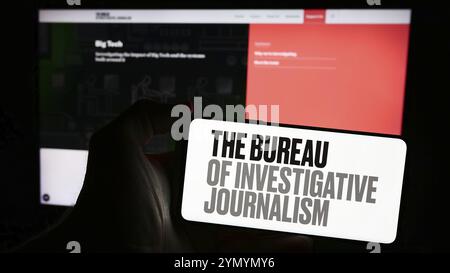 Stoccarda, Germania, 04-13-2024: Persona con smartphone e logo dell'organizzazione il Bureau of Investigative Journalism (TBIJ) di fronte al sito web. Foto Stock