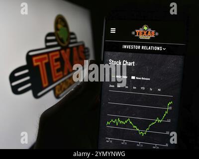 Stuttgart, Germania, 03-13-2024: Persona che tiene il cellulare con pagina web della società di ristoranti grill statunitense Texas Roadhouse Inc. Davanti al logo. Concentrati Foto Stock