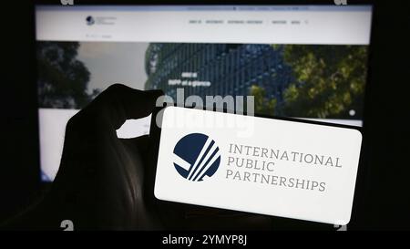 Stoccarda, Germania, 03-20-2024: Persona che possiede uno smartphone con il logo della società britannica International Public Partnerships Limited davanti al sito web. Foto Stock