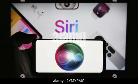 Stoccarda, Germania, 05-24-2024: Persona che tiene il cellulare con il logo del software di assistente digitale Siri (Apple Inc.) davanti alla pagina web aziendale. Concentrati Foto Stock