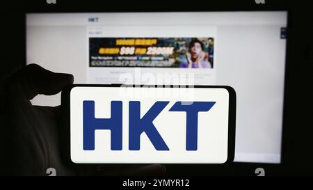 Stoccarda, Germania, 04-13-2024: Persona che detiene un cellulare con il logo della società di telecomunicazioni HKT Limited (Hong Kong Telecom) davanti alla pagina web. Foto Stock