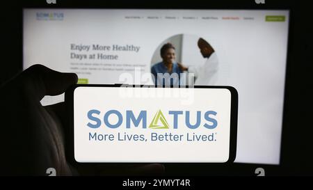 Stoccarda, Germania, 07-12-2024: Persona che detiene il cellulare con il logo della società statunitense Somatus Inc. Di fronte alla pagina web aziendale. Concentrati sul telefono Foto Stock