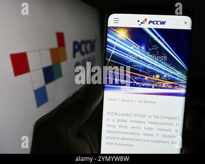 Stoccarda, Germania, 03-17-2024: Persona che possiede uno smartphone con pagina web della società di telecomunicazioni PCCW Limited davanti al logo aziendale. Concentrati su Foto Stock