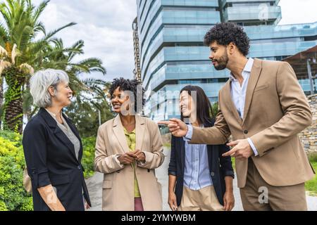 Uomo d'affari che parla con clienti donne multietniche fuori da un edificio finanziario della città Foto Stock