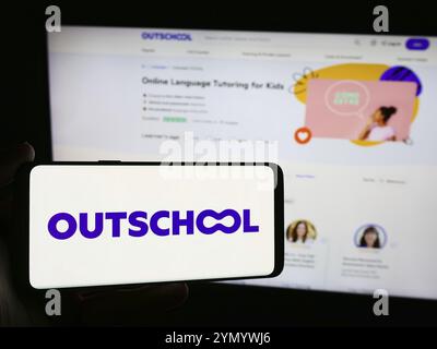 Stoccarda, Germania, 06-12-2024: Persona con smartphone con logo della società di formazione online statunitense Outschool Inc. Davanti al sito Web. Concentrati sul telefono Foto Stock