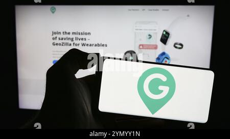 Stuttgart, Germania, 02-24-2024: Persona che possiede un telefono cellulare con il logo della società americana di localizzazione GPS GeoZilla Inc. Davanti alla pagina web. Fil Foto Stock